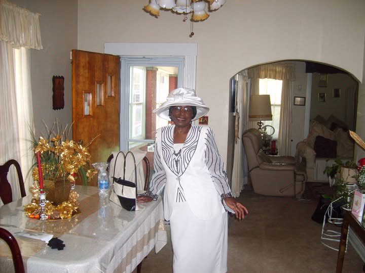 Minnie Linzy in white, smiling in her dining room